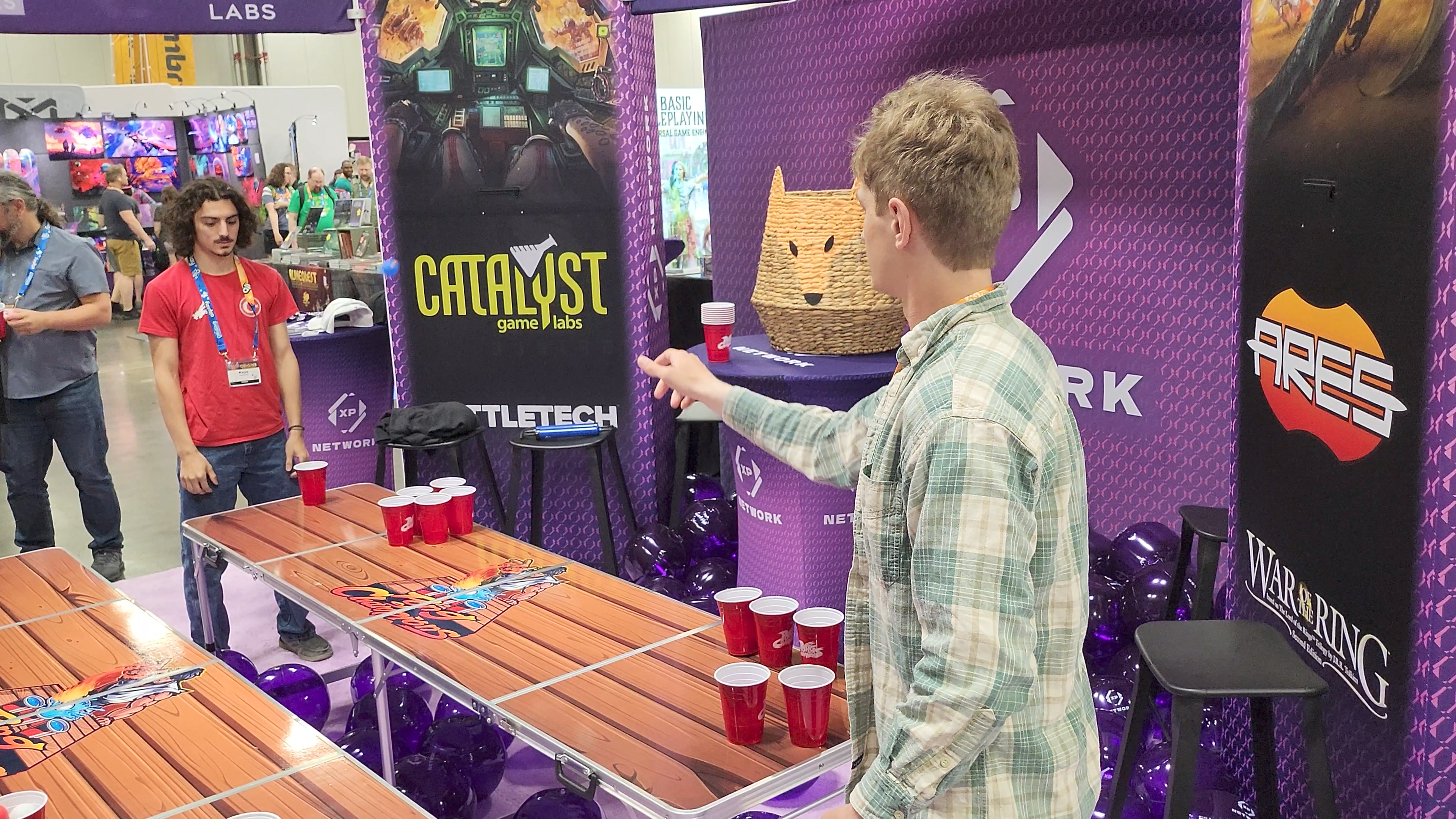 Inside the XP Network booth, two players are locked in a tense 1v1 game of cup pong. One side has just a single cup remaining, while the other side has two, making it a close and dramatic finish.